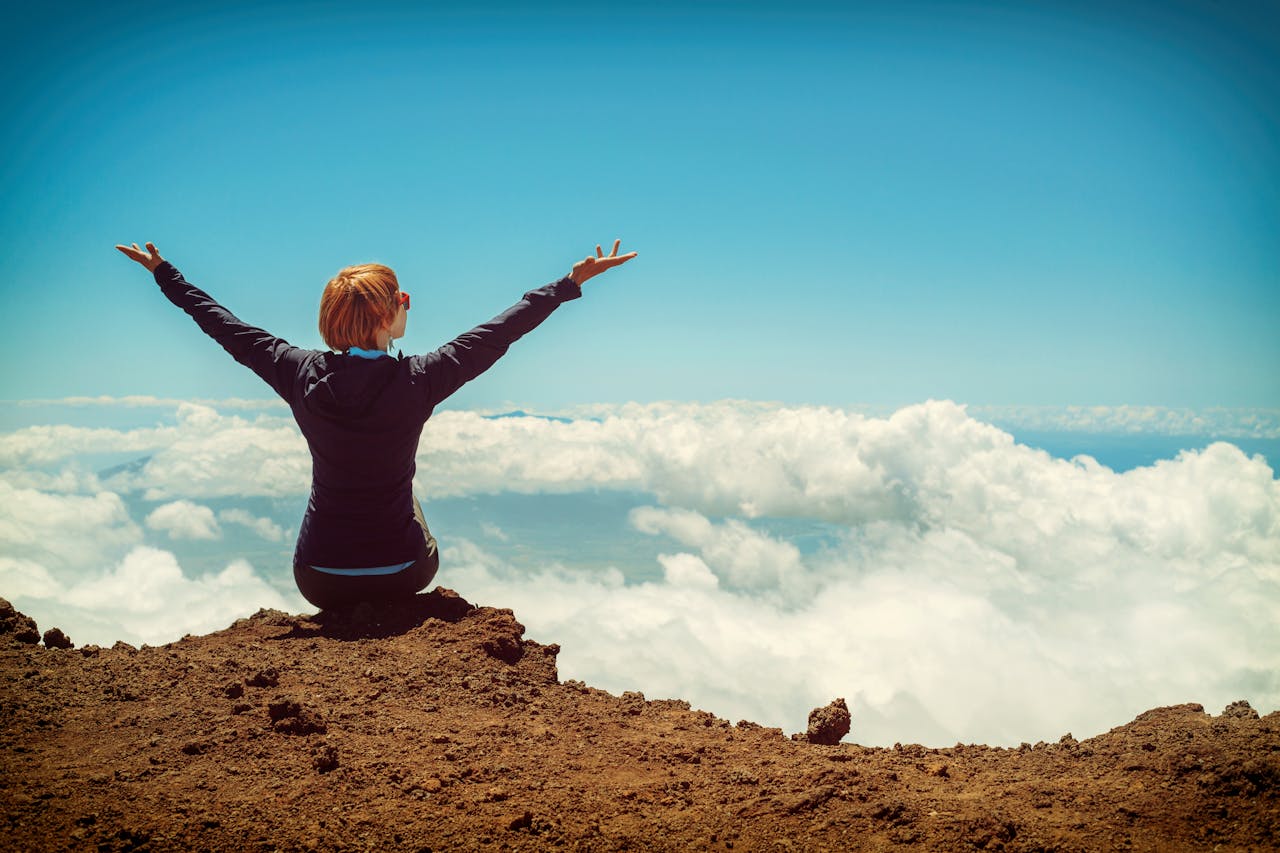 about-us A woman enjoys a scenic view atop a cliff in Kula, Hawaii, surrounded by clouds and blue sky.